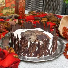 A chocolate-decorated cake with whipped cream and chocolate leaves on top, set on a silver platter.