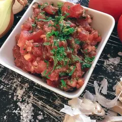 En skål med färsk tomatsalsa, redo för ett tomatsalsa recept. Ingredienser som lök, vitlök och tomater syns runt omkring.