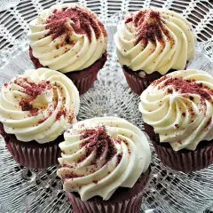 Fem röda sammetscupcakes med fluffig vit frosting, strösslade med smulor.