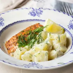 En bit stekt lax med citron och en generös portion krämig dillstuvad potatis på en vacker blåvit tallrik.