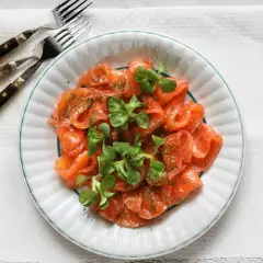 En tallrik med gravad lax, garnerad med dill och gröna blad. Perfekt för att frysa in och njuta av senare.