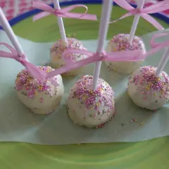 Sju cake pops med vit choklad och rosa strössel, dekorerade med rosa band. Perfekta att frysa in för senare njutning.
