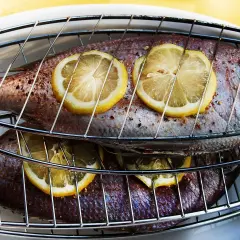 Två hela fiskar ligger på ett grillgaller, toppade med citronskivor. Snart är det dags att grilla fisk!