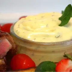 En skål med falsk bearnaisesås kall, bredvid en saftig köttbit, körsbärstomater och en halverad jordgubbe.
