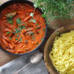 En krämig korv stroganoff med morötter i en panna, bredvid en skål med färsk pasta.