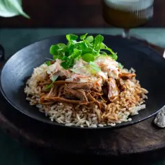 En tallrik med pulled pork med ris, toppad med krispig coleslaw och gröna blad. En härlig måltid som ser utsökt ut.