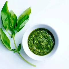 En skål med hemgjord pesto bredvid färska basilikablad. Perfekt för ditt nästa pesto recept!