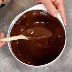 En sked rör i en skål med glansig choklad. Perfekt för ett enkelt ganache recept.