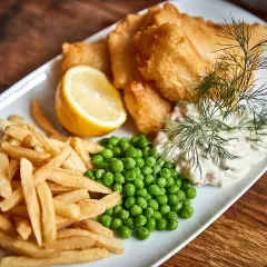 En tallrik med krispigt fish and chips, ärtor, citronklyfta och dill.