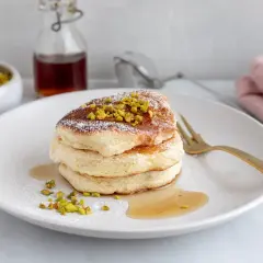 Fluffiga japanska pannkakor toppade med pistagenötter och pudersocker, serverade med sirap.