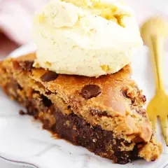 En saftig bit av en brownie-cookie-kaka med blockchoklad, toppad med vaniljglass och en guldfärgad gaffel. Perfekt att baka med blockchoklad!