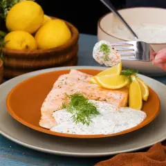 En gaffel tar en bit lax med romsås. Serverad med citron och dill.
