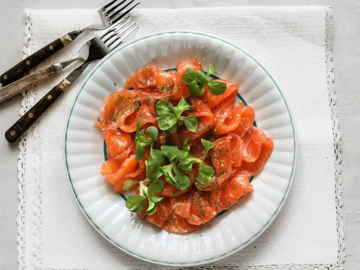 En tallrik med gravad lax, garnerad med dill och gröna blad. Perfekt för att frysa in och njuta av senare.