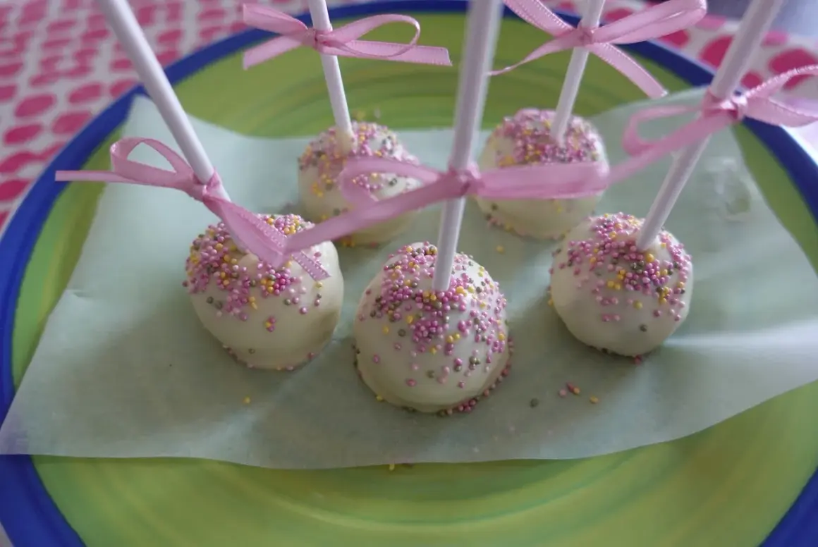 Sju cake pops med vit choklad och rosa strössel, dekorerade med rosa band. Perfekta att frysa in för senare njutning.