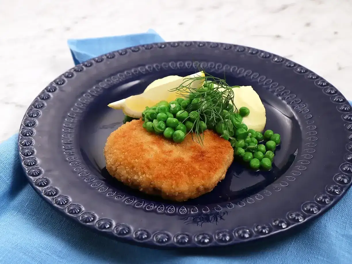 En gyllene havets wallenbergare serveras med potatis, gröna ärtor, citron och dill på en mörkblå tallrik.