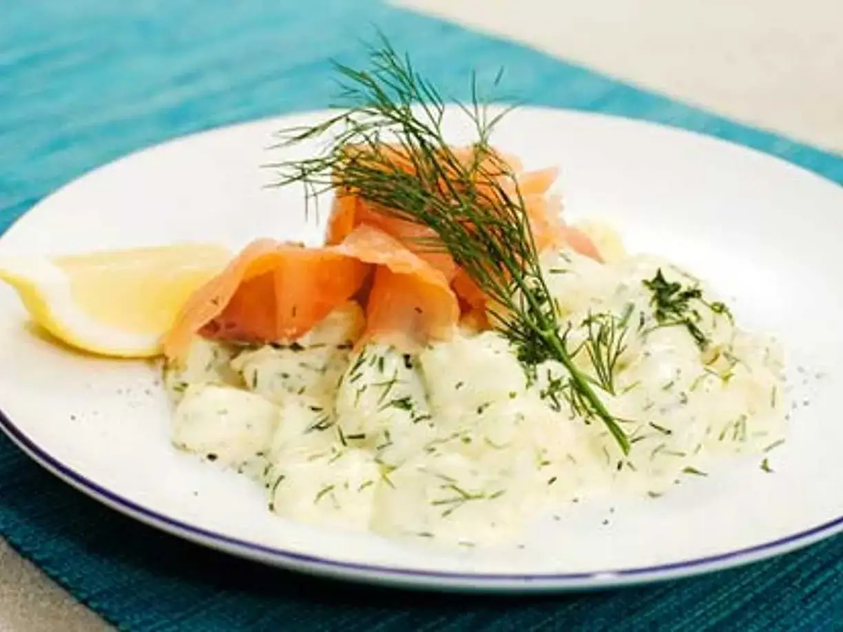 En tallrik med dillstuvad potatis, toppad med rökt lax och en citronklyfta. En klassisk svensk rätt som ser utsökt ut.
