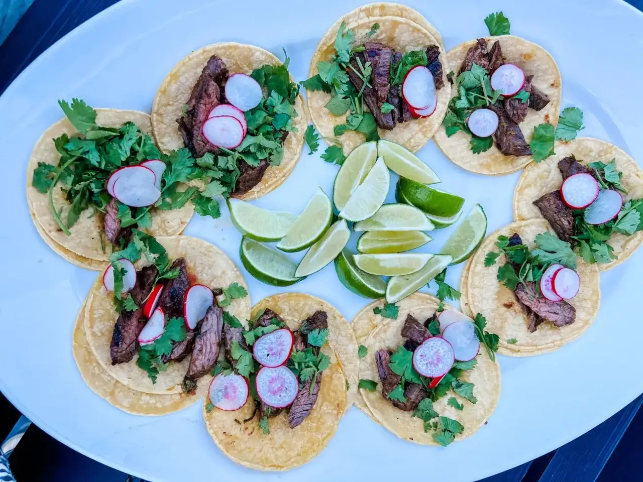 En tallrik med mexikansk tacos, fyllda med saftigt kött, färsk koriander och skivad rättika, garnerade med limeklyftor.