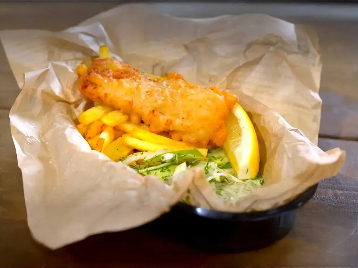 Krispig fish and chips med pommes frites, citronskiva och en fräsch sallad, serverad i brunt papper.