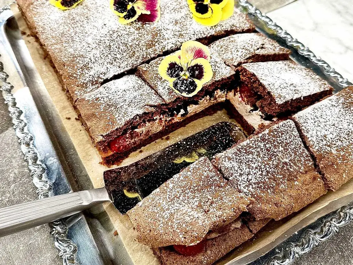 Enkel tårta choklad med vispgrädde och jordgubbar, pudrad med florsocker och dekorerad med penséer.