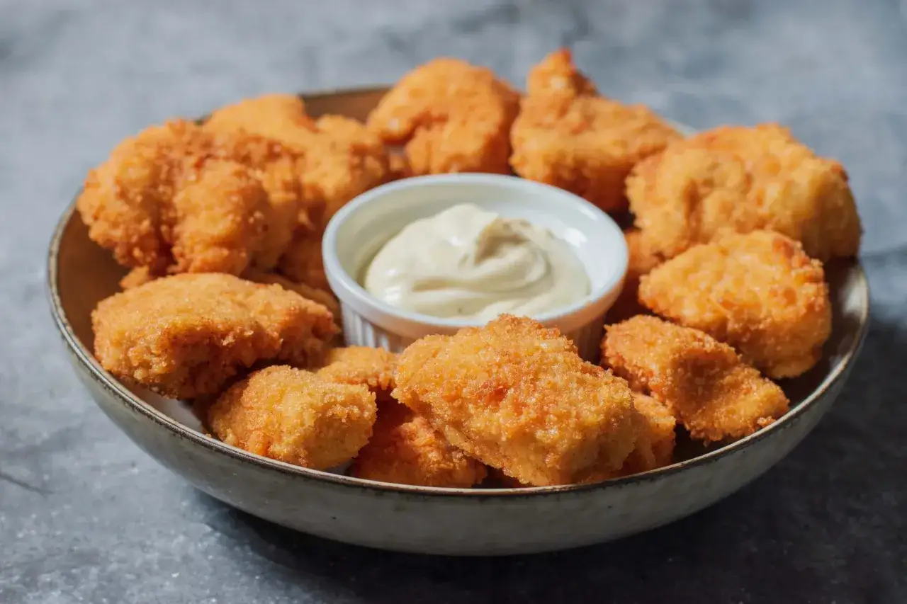 En skål med gyllene, krispiga chicken nuggets och en liten skål med dippsås. Perfekt för en snabb och god måltid.